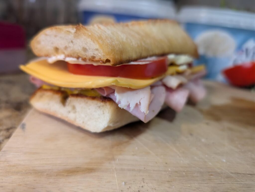 Ham, chicken, and mortadella on a toasted ciabatta bun with mustard, mayonnaise, and tomato.