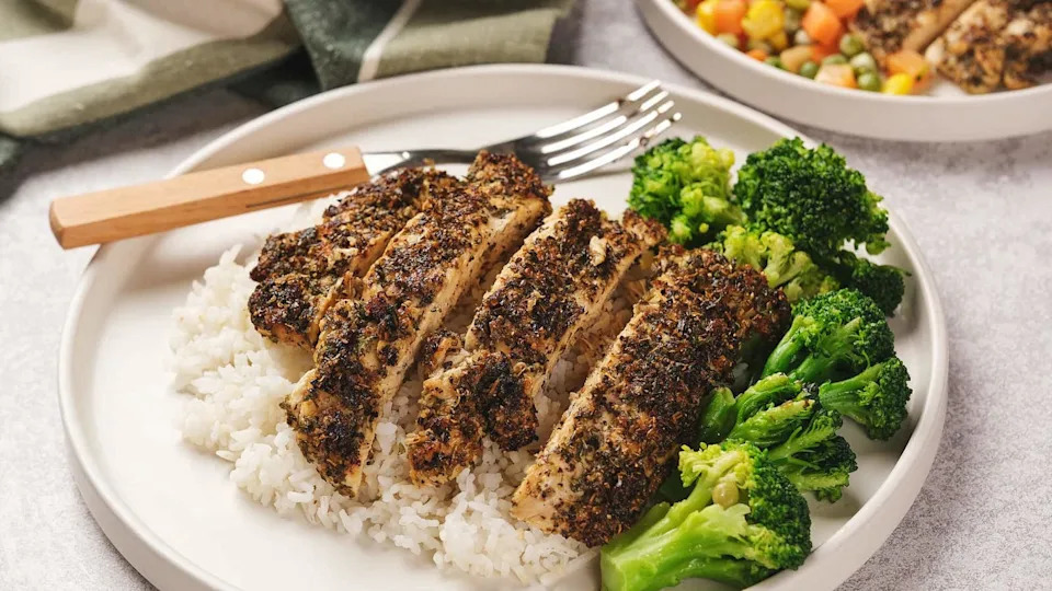 A plate with sliced herb-crusted chicken on rice, accompanied by broccoli.