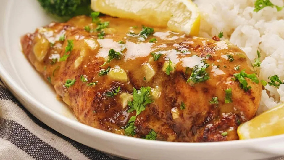 Honey mustard chicken with lemon glaze, garnished with parsley, served alongside white rice and broccoli on a white plate.