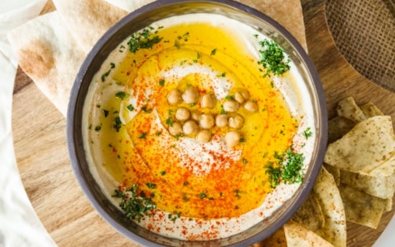 A bowl of hummus surrounded by slices of pita bread at Meddys