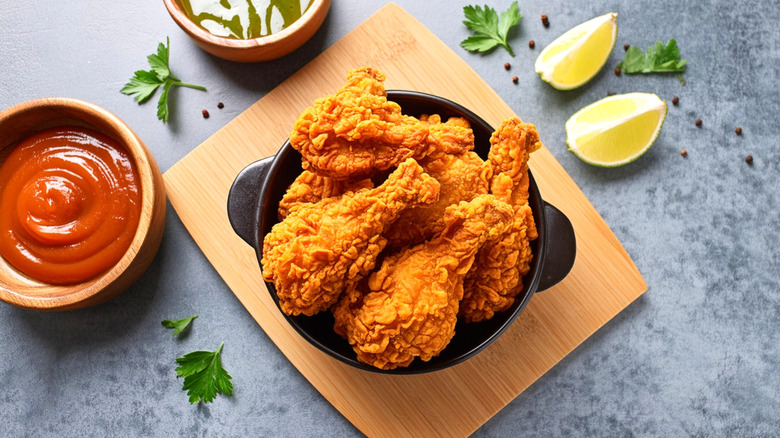 A bowl of beautifully golden fried chicken is placed on a cutting board.