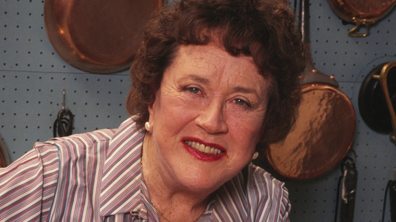 Closeup of Julia Child in front of a pegboard full of copper pans