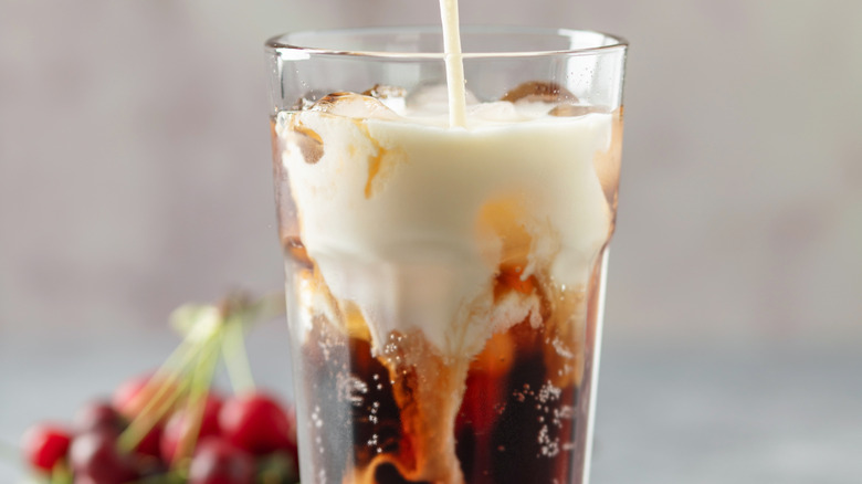 Cream pouring into a dirty soda with cherries in background