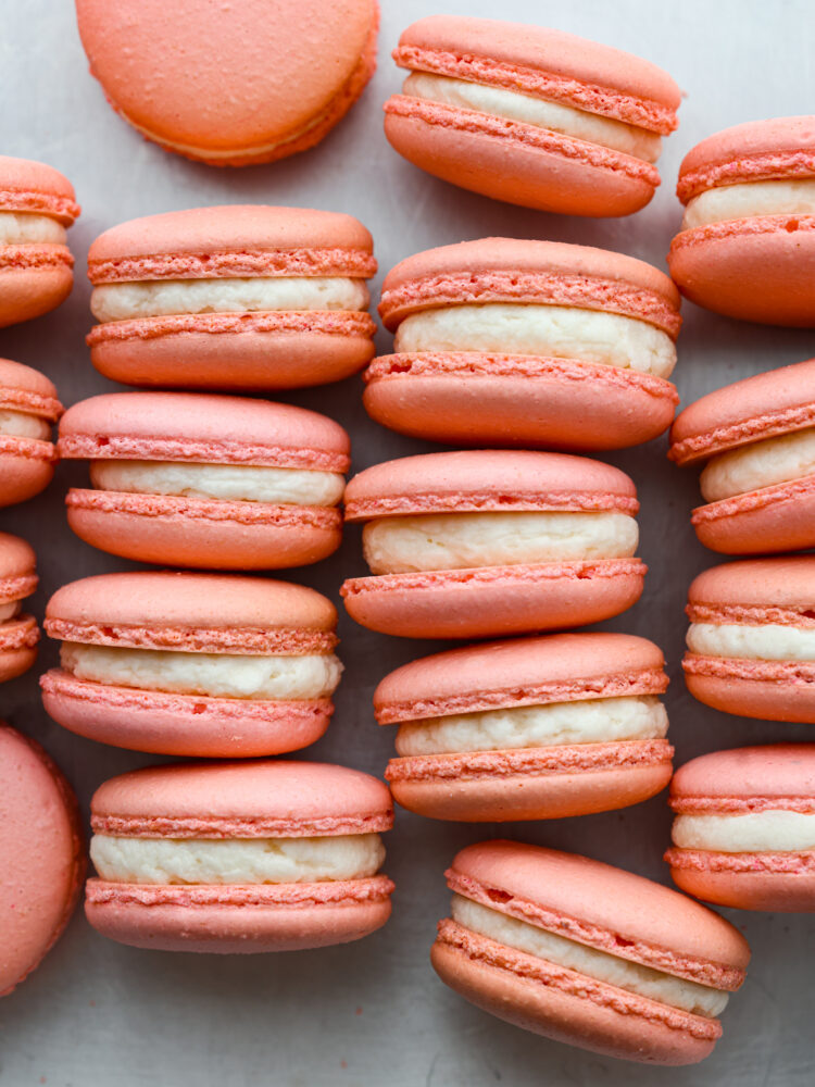 This French macaron cookie recipe makes the perfect macaron every time! I share all of my tips and tricks to get the perfect feet on your macaron, and a delicate and airy cookie with a shiny smooth shell. You are going to love making these fun and elegant cookies at home! Macarons on a table stacked up next to each other with white frosting.
