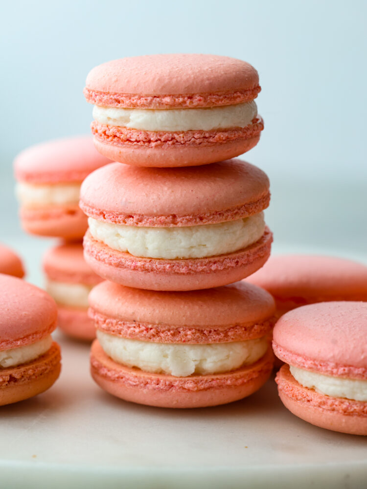 This French macaron cookie recipe makes the perfect macaron every time! I share all of my tips and tricks to get the perfect feet on your macaron, and a delicate and airy cookie with a shiny smooth shell. You are going to love making these fun and elegant cookies at home! Three macarons stacked on top of each other with other macarons around it.