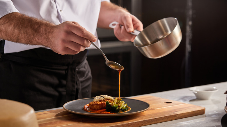Chef spooning sauce over plated meat and veggie dish