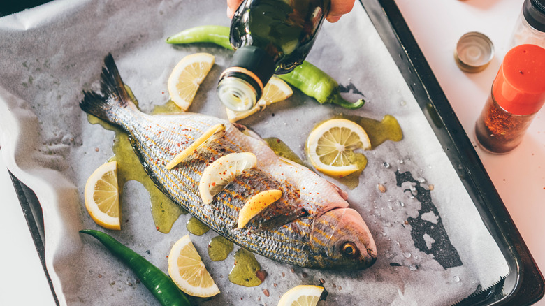 Person using olive oil on fish with lemons and peppers