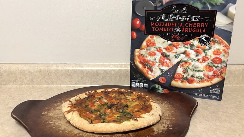 Mozzarella, cherry tomato, and arugula pizza on baking stone and box on a neutral background.