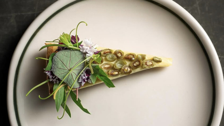 A slice of tart topped with fresh herbs and edible flowers