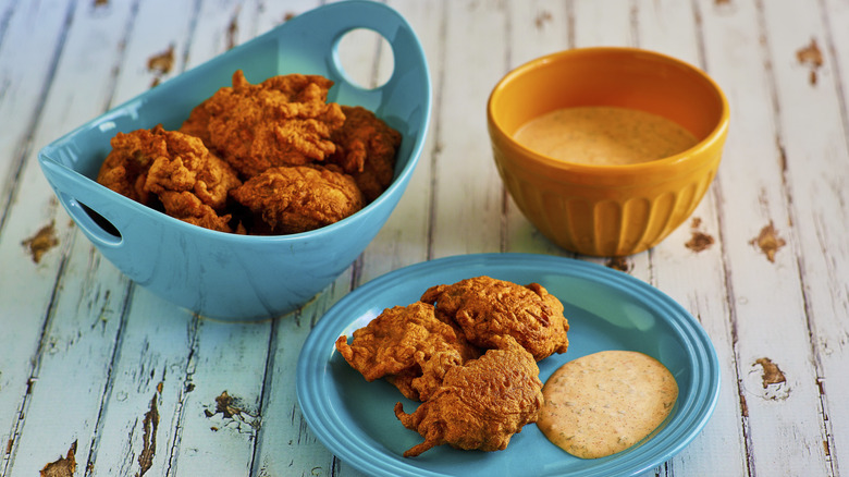 Conch fritters in blue dishes next to spicy sauce on white wooden table