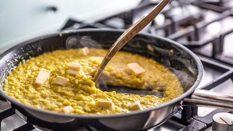 Person stirring risotto with butter in pan on stove