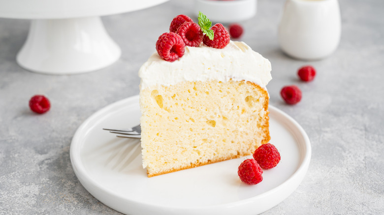 Square slice of tres leches cake, with vanilla sponge cake topped with whipped cream and garnished with fresh raspberries and a mint sprig