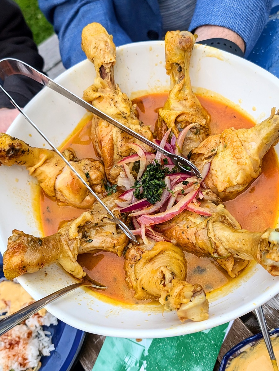 Hands hold a big white plate full of chicken thighs in an orange sauce, topped with red onions and herbs.