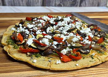 Socca, a chickpea flatbread, is covered in chermoula and healthy roasted veggies with feta cheese on top.