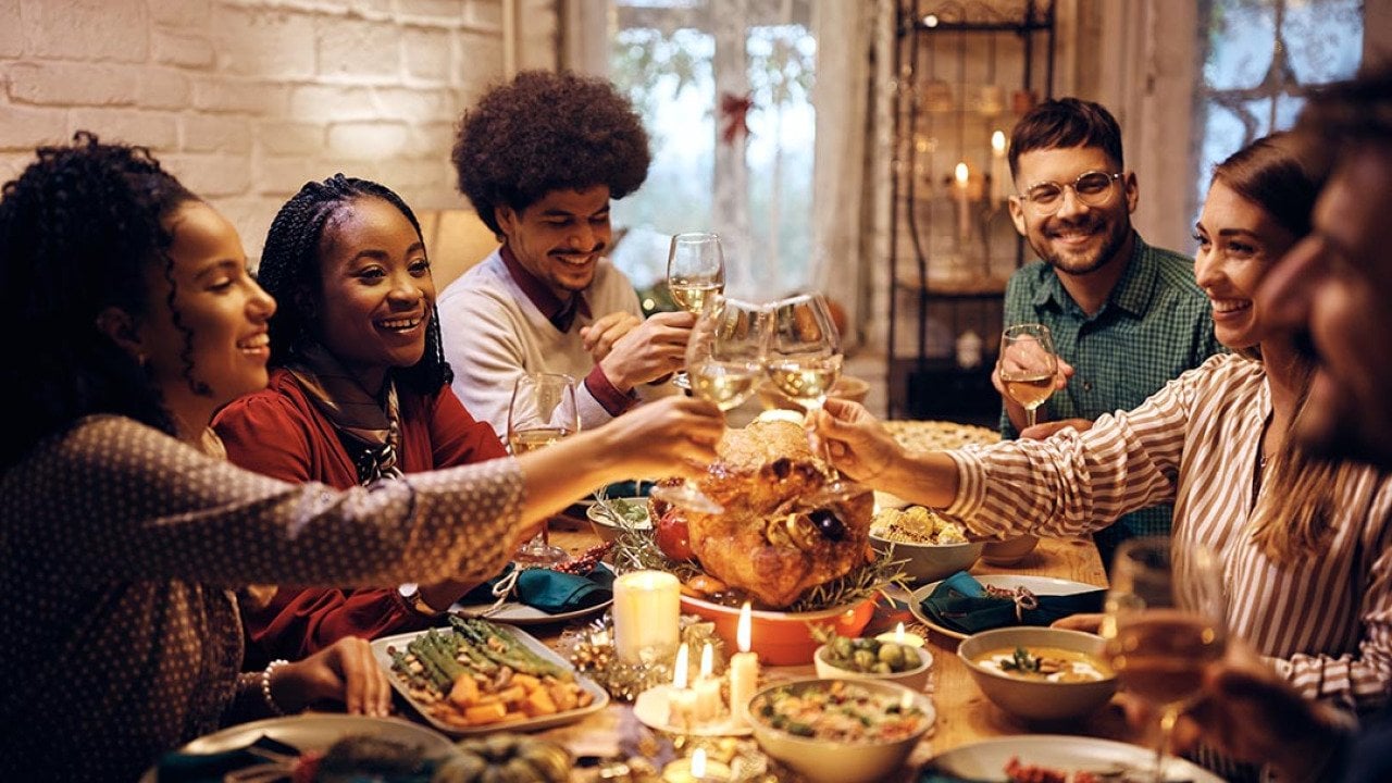 Group of diverse young people toasting at dining table while celebrating Thanksgiving at home. 