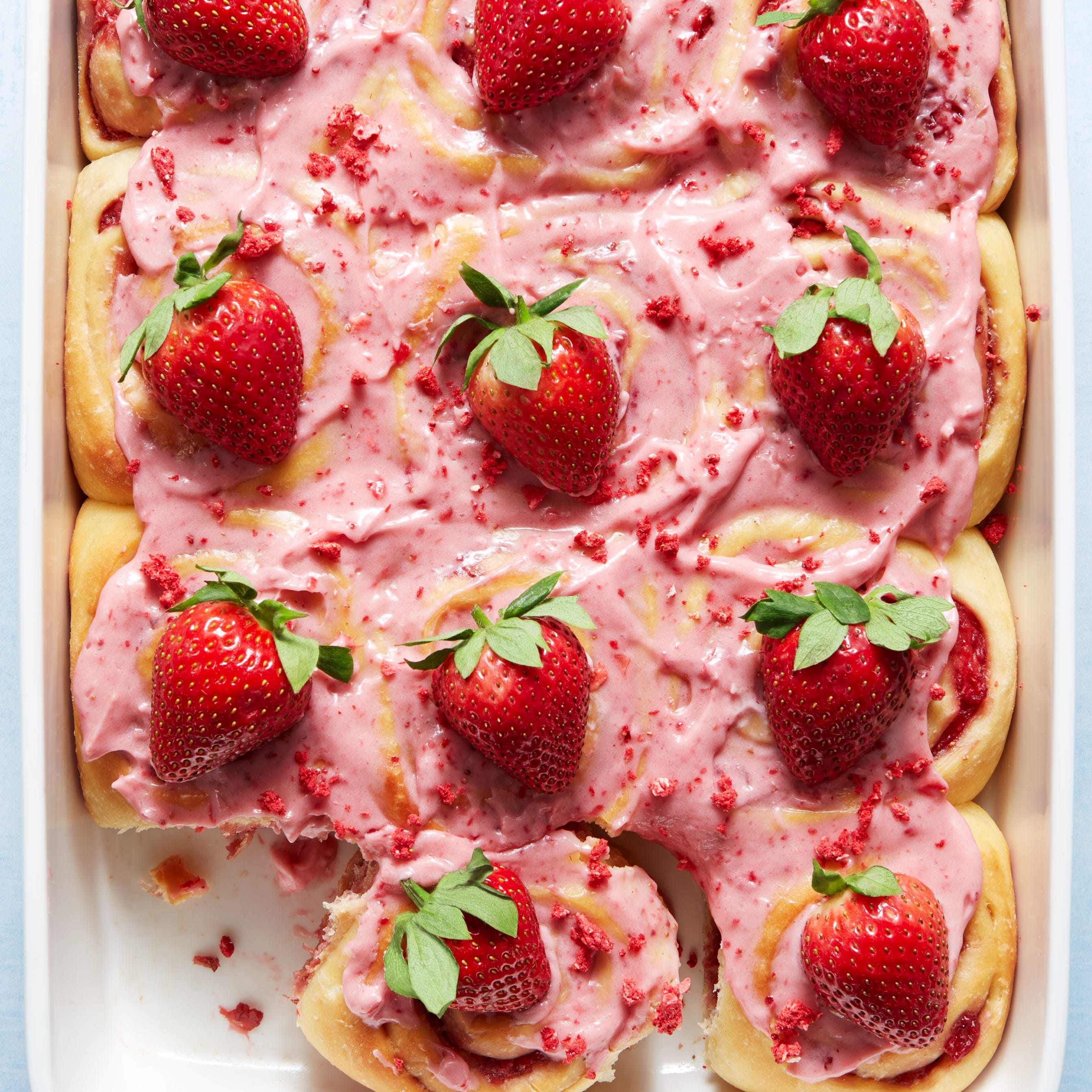 cinnamon rolls topped with strawberry frosting, crunch pieces, and strawberries