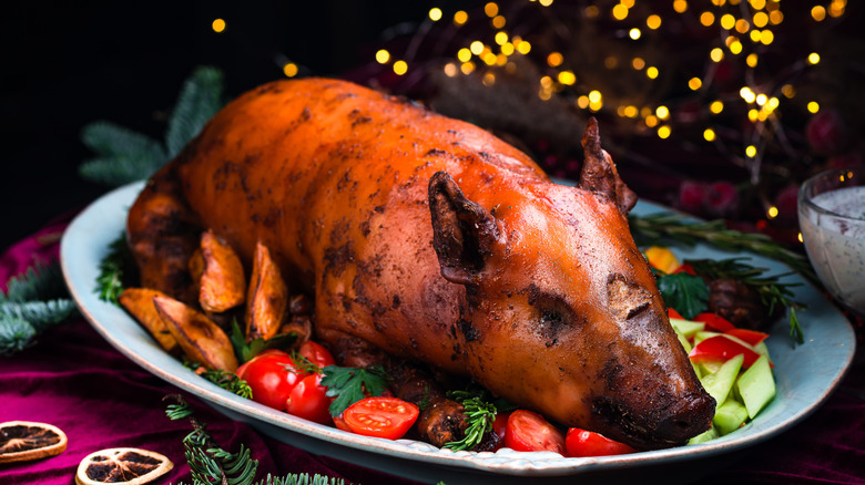 Roast suckling pig on a platter surrounded by vegetables