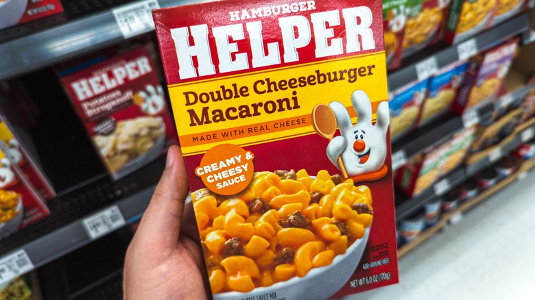 A hand holding a box of double cheeseburger macaroni Hamburger Helper in a grocery store aisle