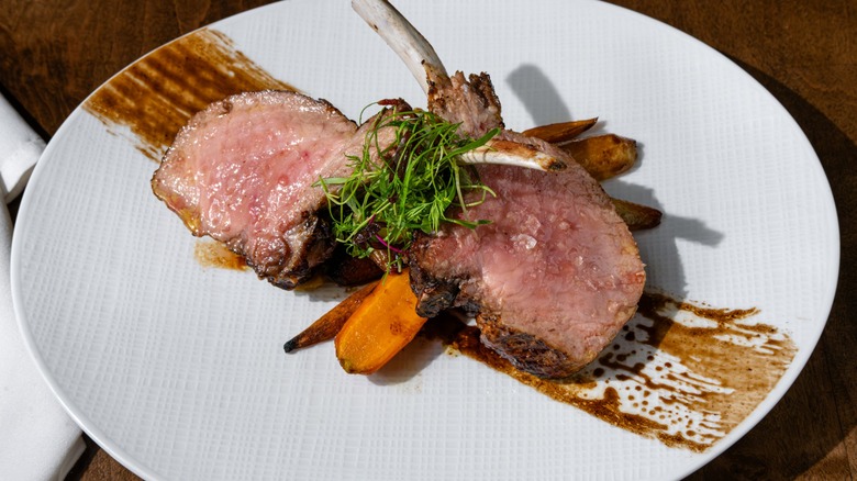 Slices of tender beef with roasted carrots, microgreens, and balsamic glaze on a white plate