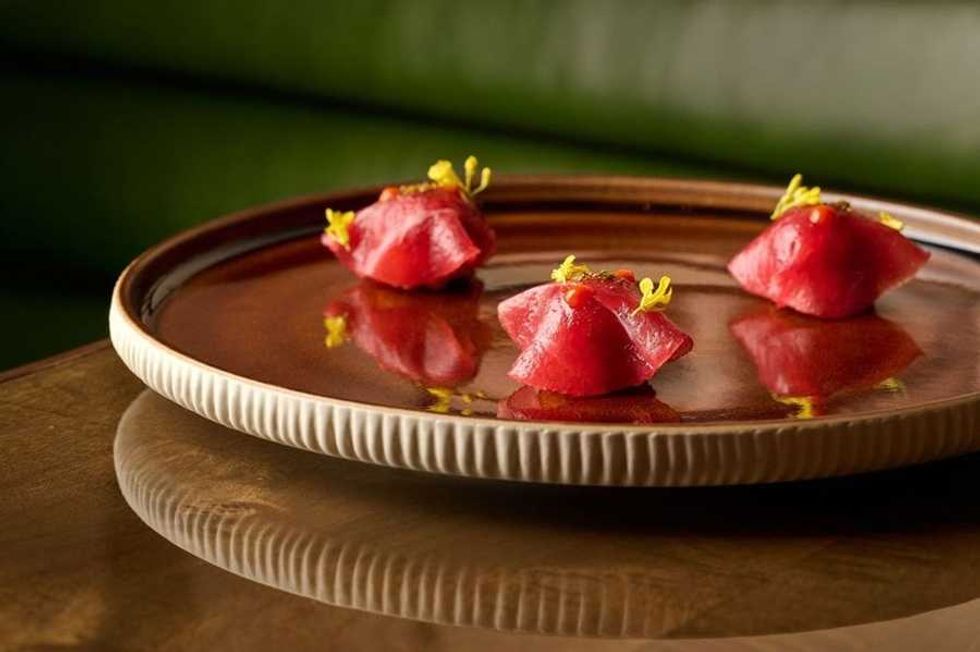 Three pieces of artistic sushi garnished on a brown ceramic plate.