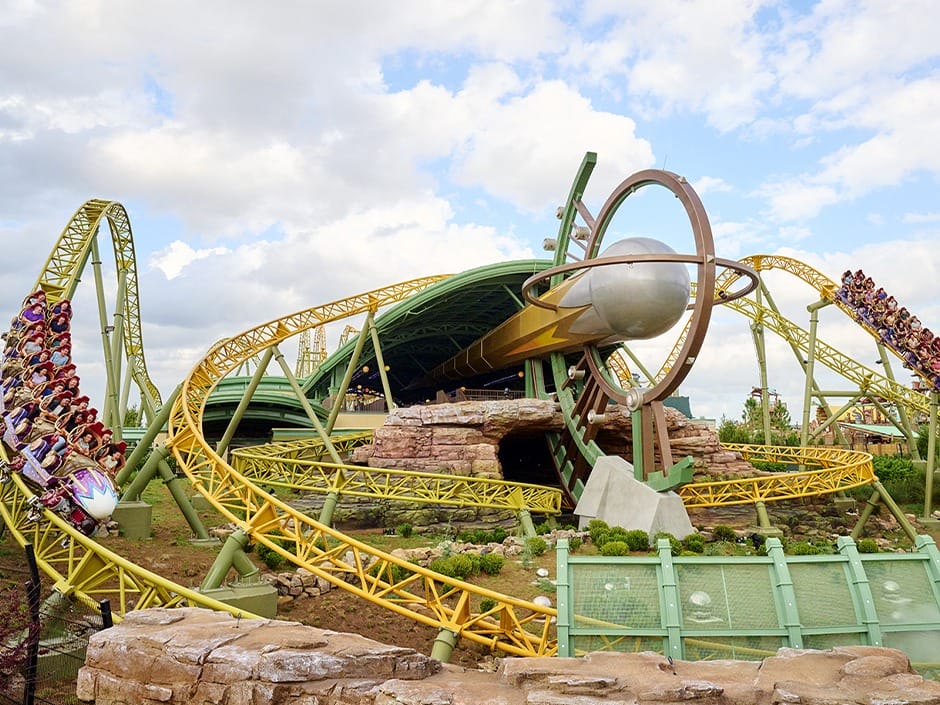 Roller coaster with yellow tracks loops around a rocket, echoing Celestial Park lore at Epic Universe under cloudy skies.