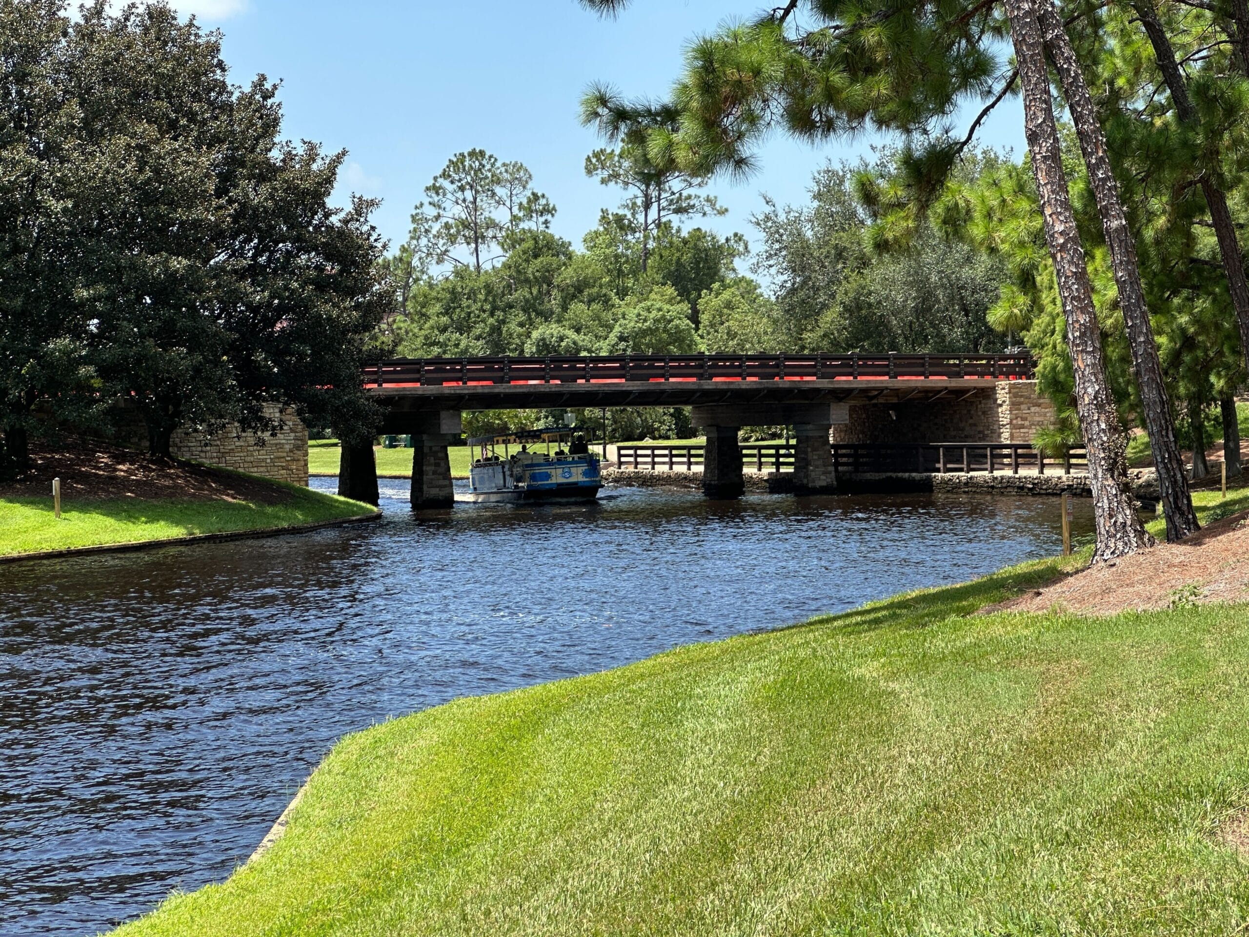 A small blue boat passes under a red bridge on a canal as the bridge reopens to traffic.