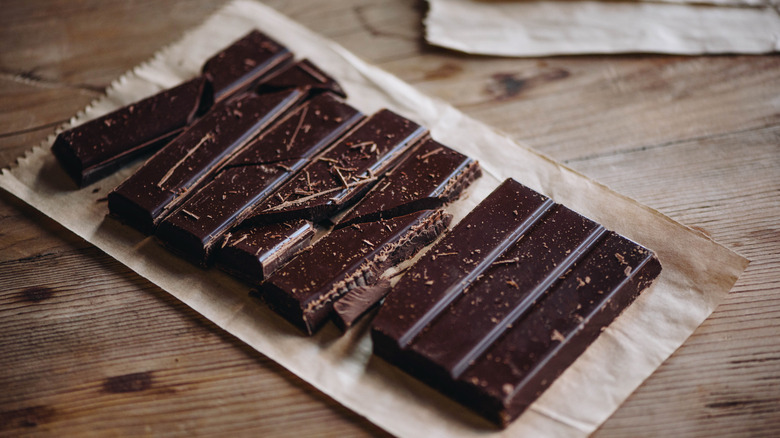 A row of dark chocolate bars with loose bits on top, on butcher paper on a wood table