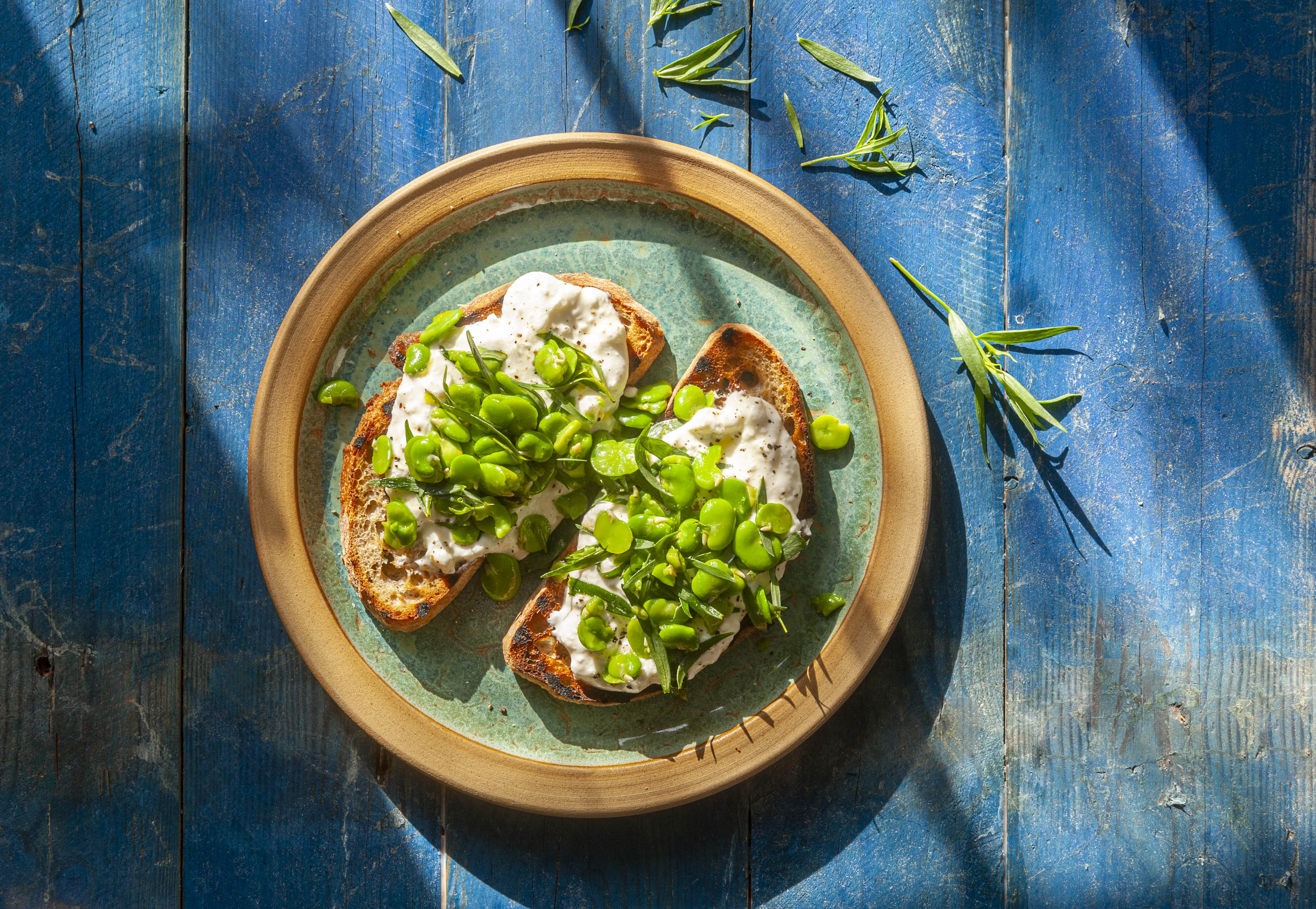 Broad beans with feta cheese on sourdough bruschetta garnished with fresh tarragon.