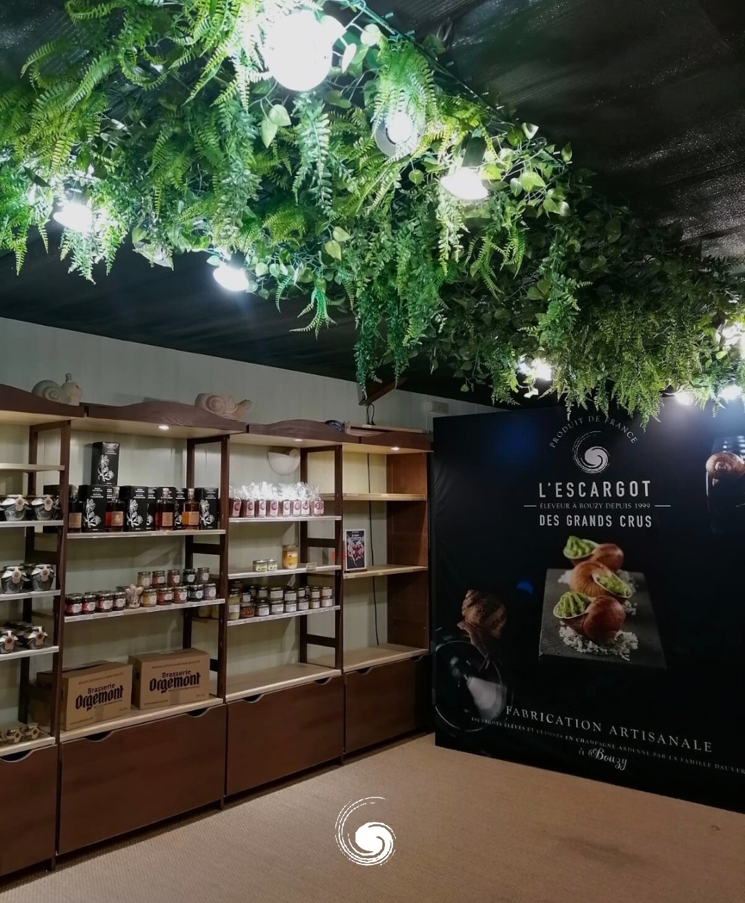 A store interior with shelves of jars and bottles and a large black banner advertising "L'Escargot des Grands Crus."