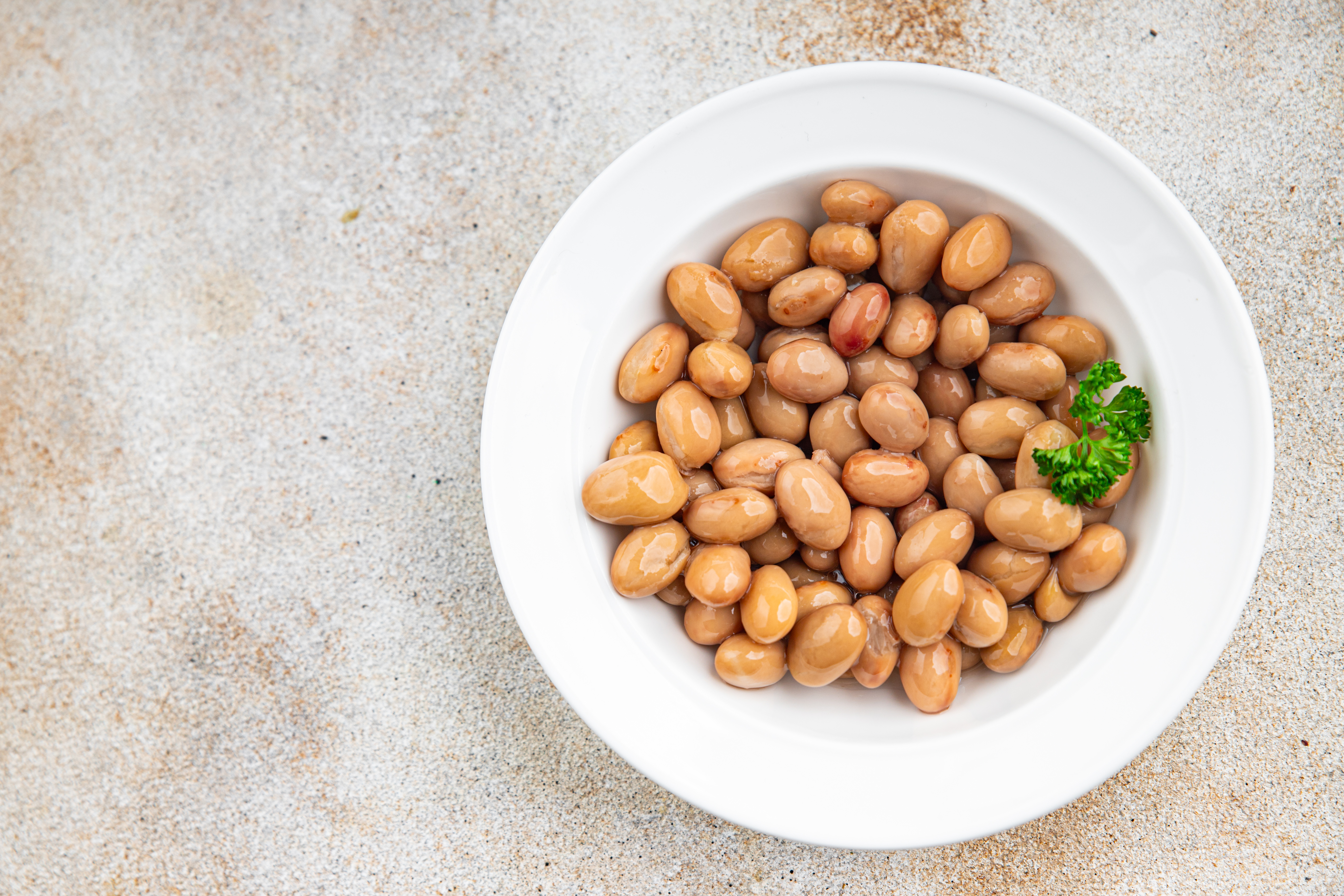 Borlotti beans in a white bowl with a sprig of parsley.