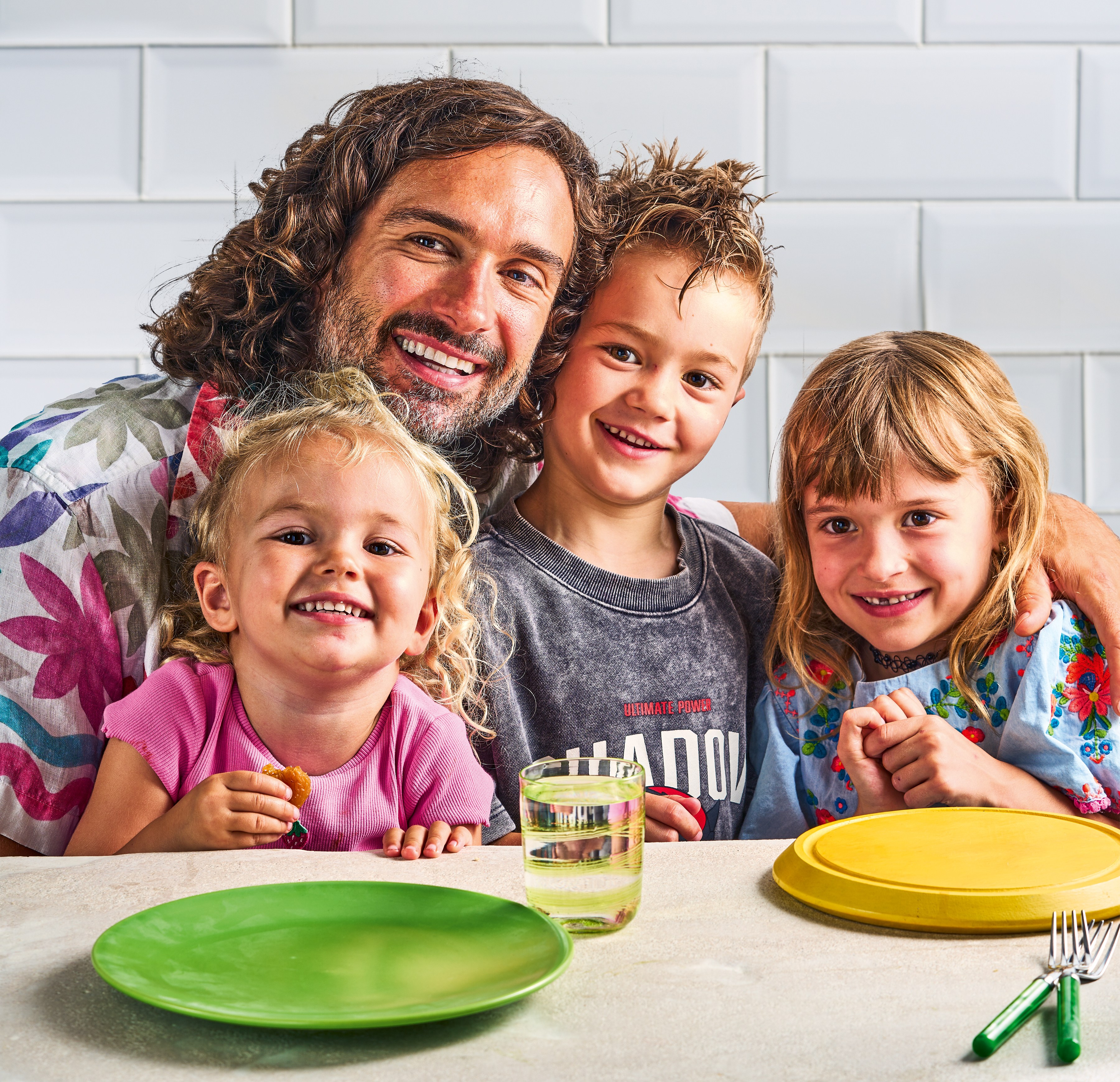 Joe Wicks posing with his three children at a table.