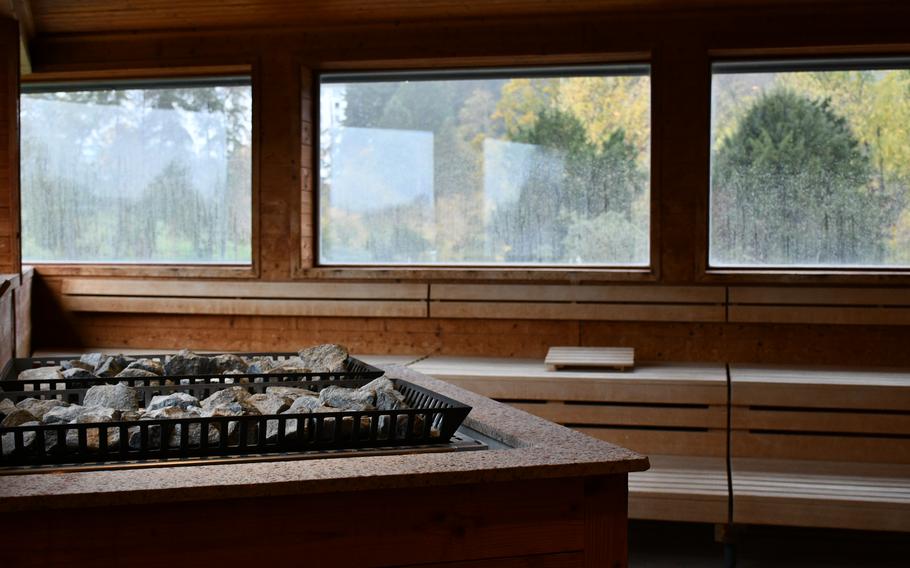 Inside a sauna at the Südpfalz Therme, wooden benches face three large windows framing a view of forested mountains and autumn foliage.