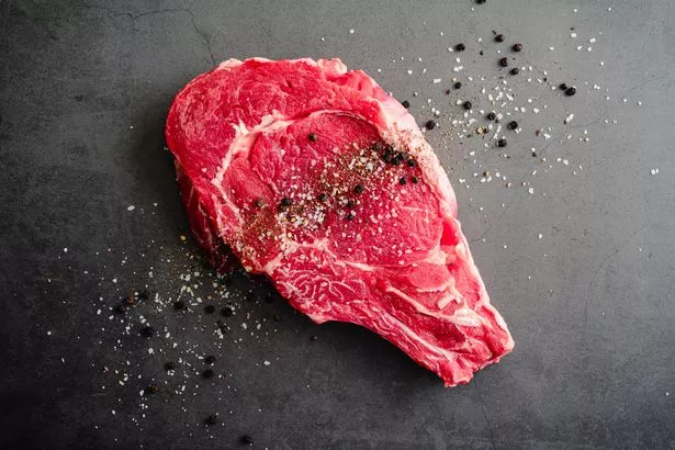 An uncooked bone-in beef steak sprinkled with salt and pepper on a dark background