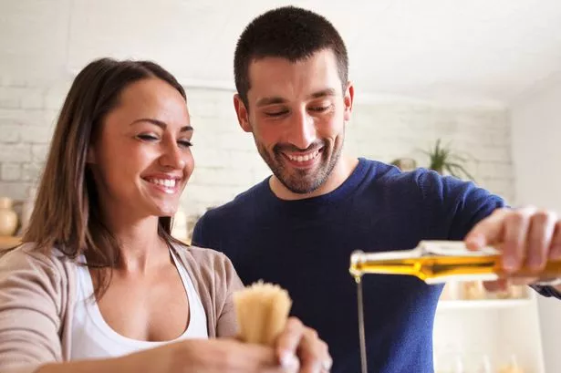 A couple cooking and pouring olive oil
