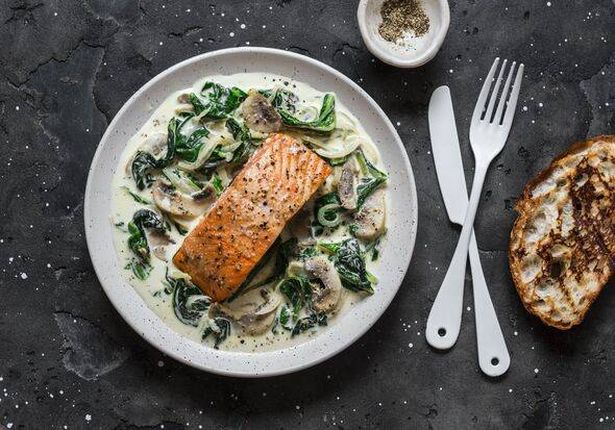 salmon with creamy spinach mushrooms sauce on a dark background, top view. Salmon florentine