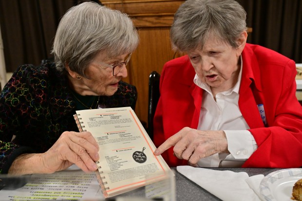 Marcia Copeland points to a cookbook that Elaine Christiansen is holding up.