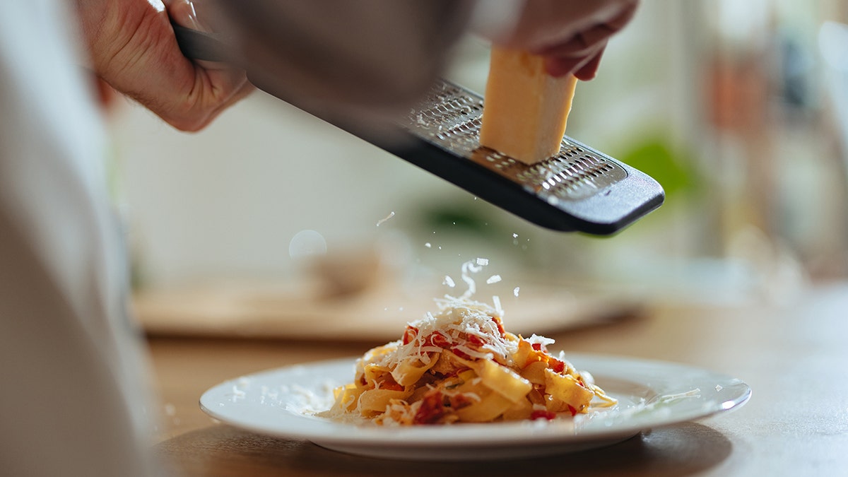 Man's hands seen up-close grating cheese on plate of pasta.