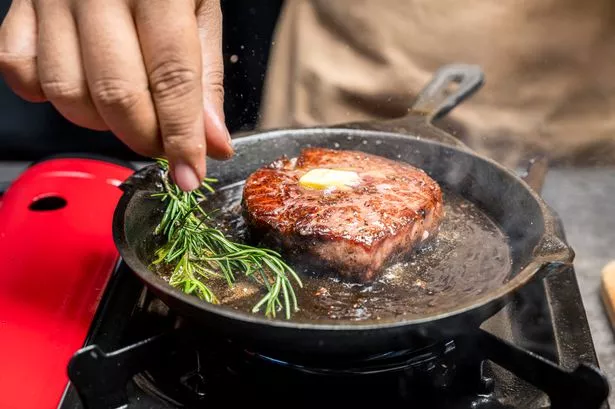 A person is cooking a tenderloin steak in a pan with butter and herbs. Concept of warmth and comfort, as the person is preparing a delicious meal