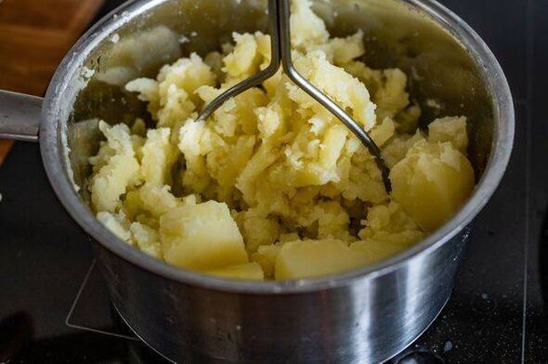 Mashing potatoes in pot on electric stove, close-up