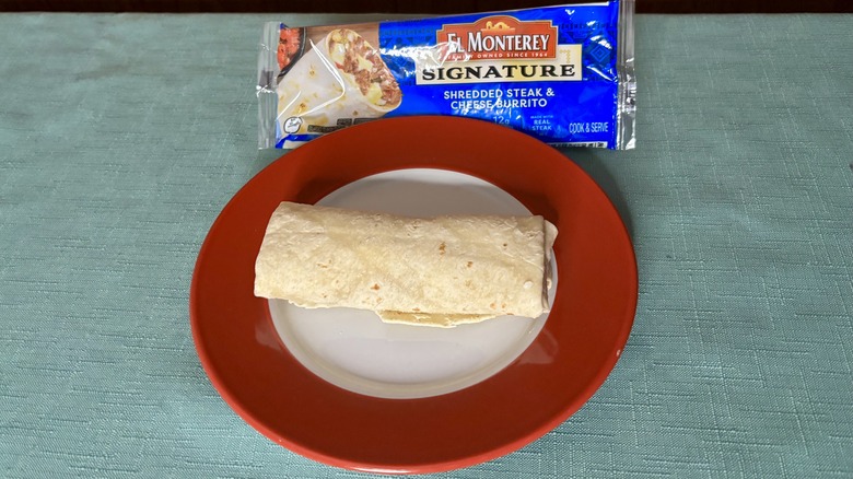 El Monterey Signature Shredded Steak & Cheese burrito on a red plate, in front of the burrito's packaging