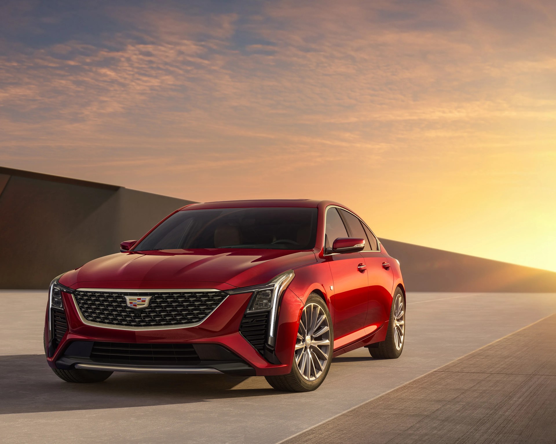 Red Cadillac sedan with chrome grille and alloy wheels parked on concrete at sunset.