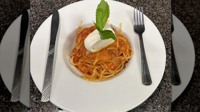 Marinara spaghetti topped with burrata and basil leaves on white plate