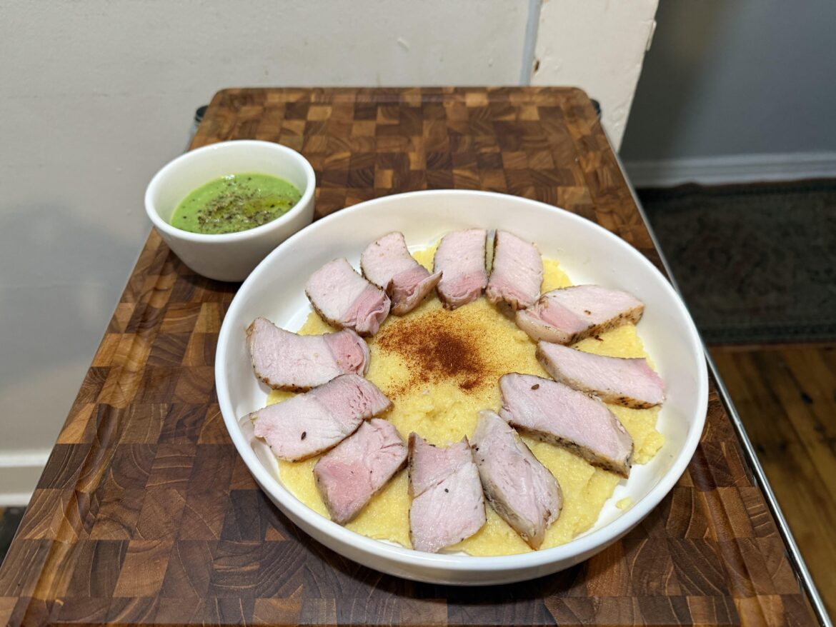 Pork chop cut from full tenderloin on a bed of polenta with broccoli soup on the side.