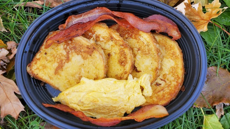 Cracker Barrel French toast with bacon and scrambled eggs in a black takeout container