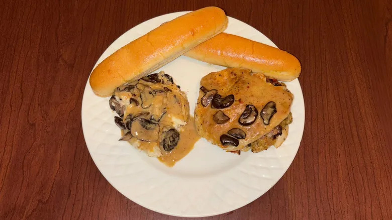 Chicken breast and mashed potatoes with mushroom gravy and breadsticks.