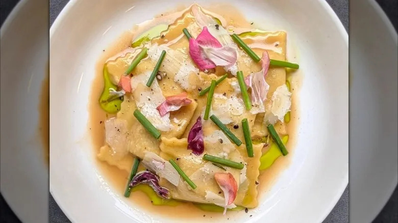 Ravioli topped with greens, flower petals, and sauce in white plate