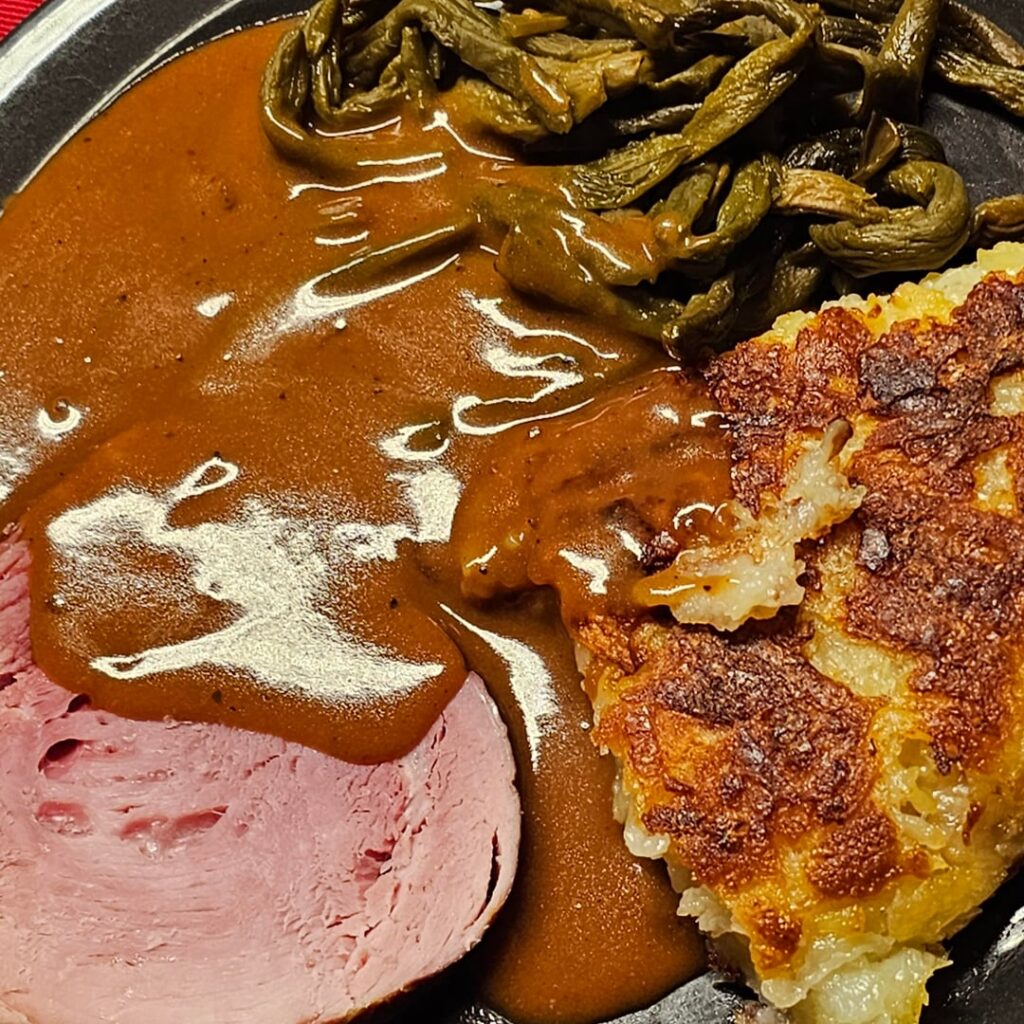 Slow-cooked Rollschinkli (smoked ham) on a bed of dried beans, served with homemade Rösti and a pepper-cream sauce