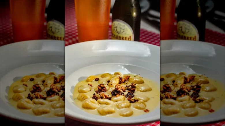 Gnocchi in cheesy cream topped with walnuts on white plate