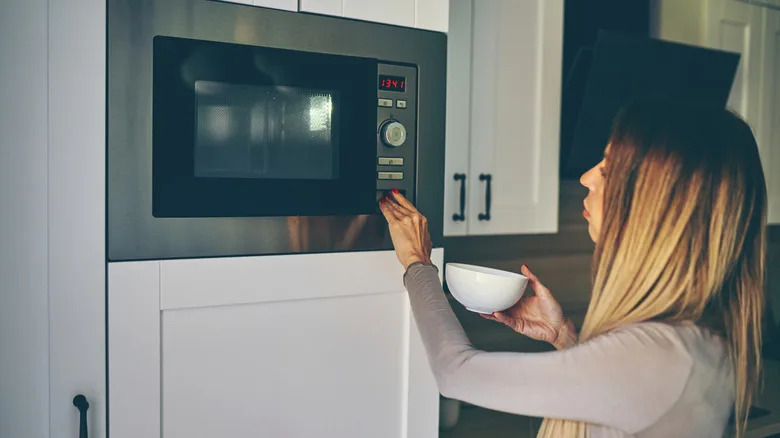 Young woman heats food in the microwave