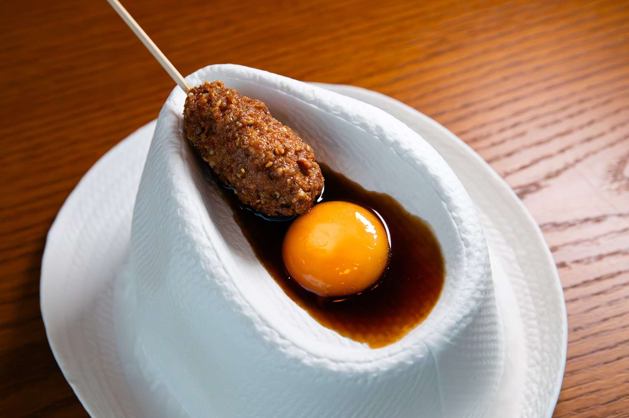A chicken meatball on a stick in a dish with egg yolk from TBD.